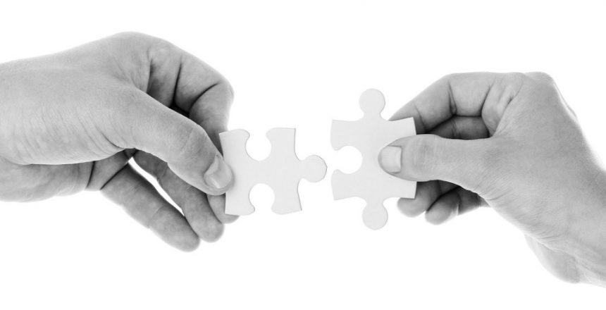 Two hands joining two puzzle pieces together.